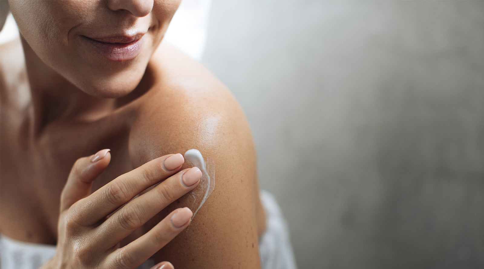 Close-up of a woman with a beautiful smile applying luxury lotion to her left shoulder.