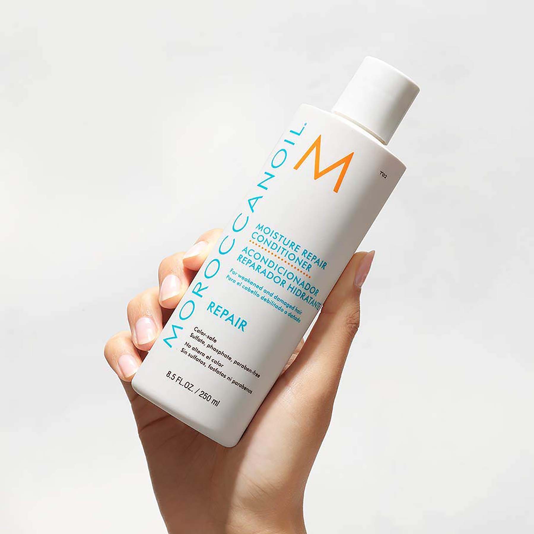 Woman right-hand holds up a Moroccanoil Moisture Repair Conditioner, 8.5 Fluid Ounces / 250 Milliliters.