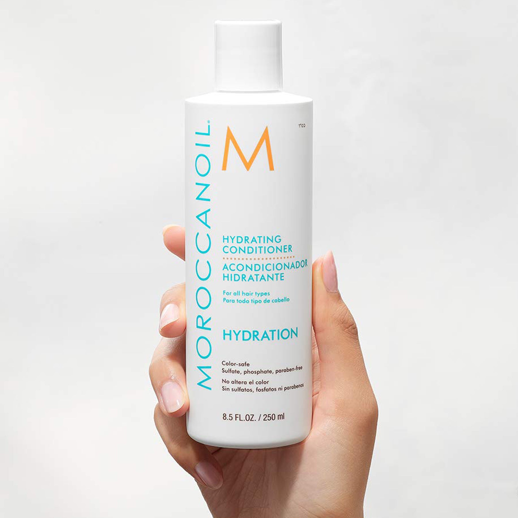 A woman right-hand holds up a Moroccanoil Hydrating Conditioner, 8.5 Fluid Ounces / 250 Milliliters.